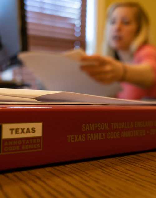 woman reads legal documents next to a red texas family code annotated book